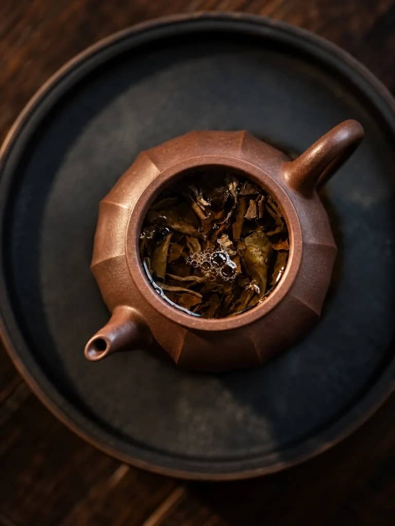 Clay teapot with steeping tea leaves on a dark tray, seen from above